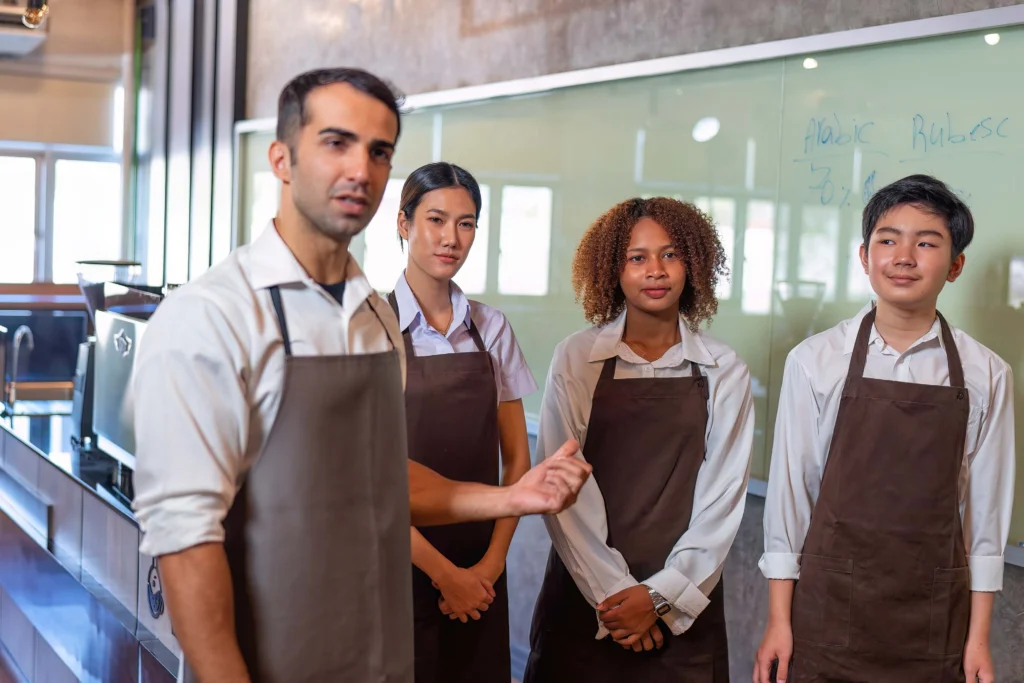 Grupo de baristas usando uniformes personalizados con mandiles color café que proyectan la imagen corporativa de la cafetería.
